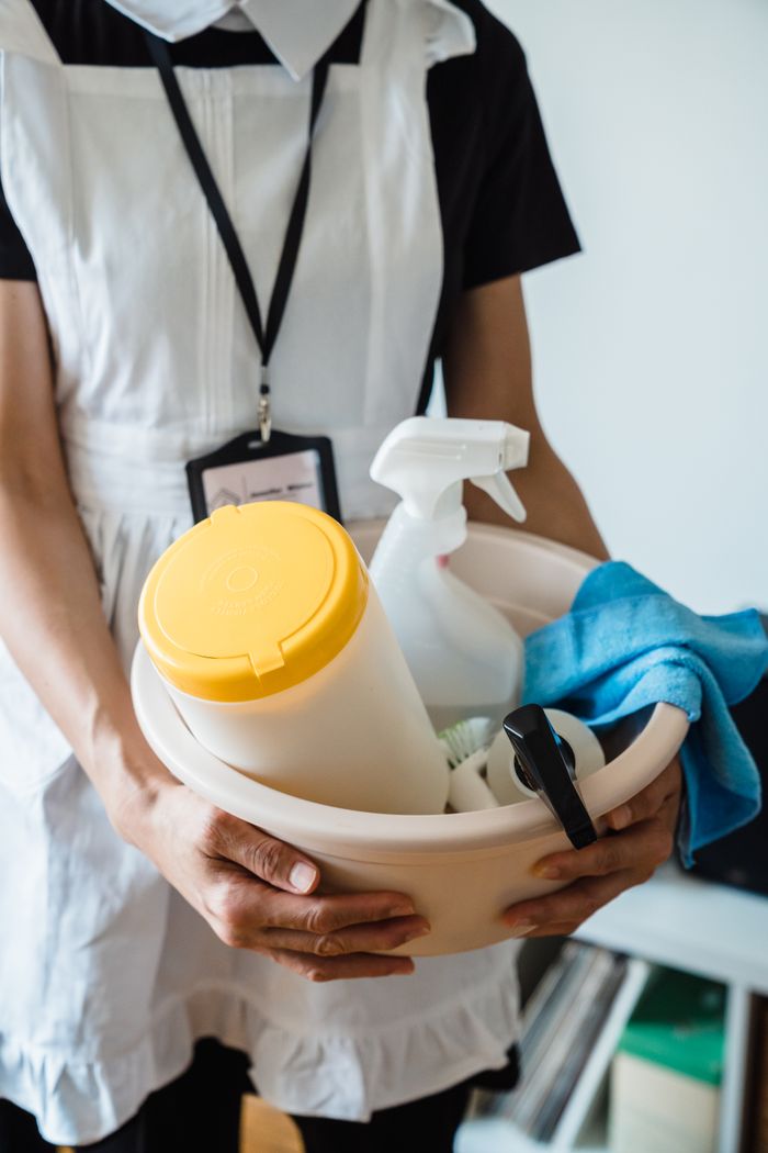 services-02 A uniformed cleaner holding a basin with cleaning supplies indoors. Ideal for cleaning and sanitation themes.