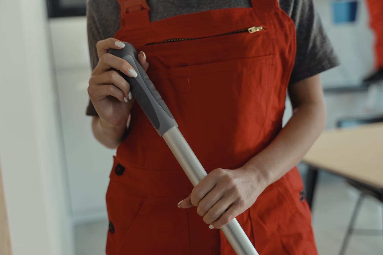 about-01 A woman in a red apron holding a mop handle, performing cleaning indoors.